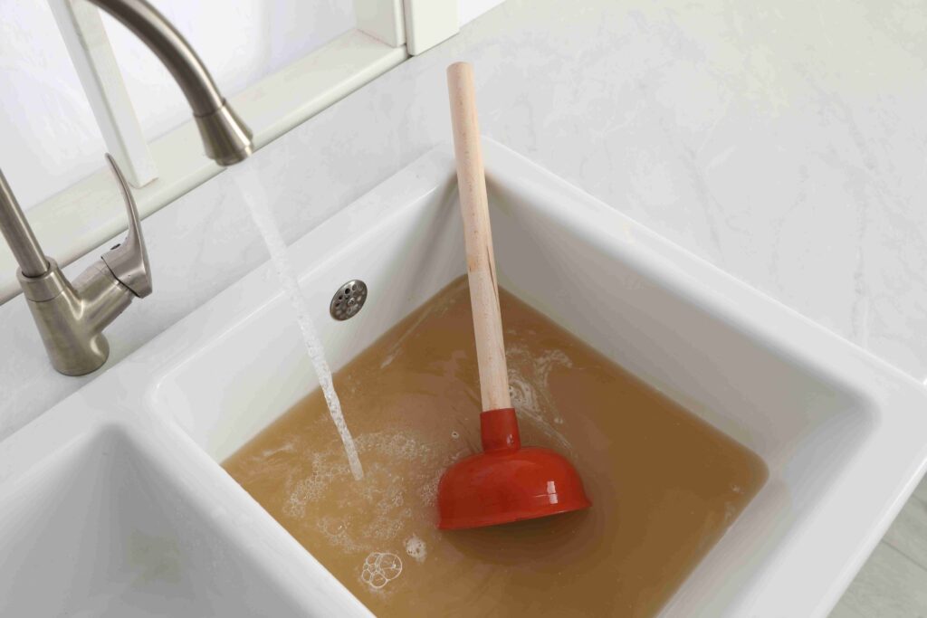 Picture of a clogged sink with red plunger and open tap.