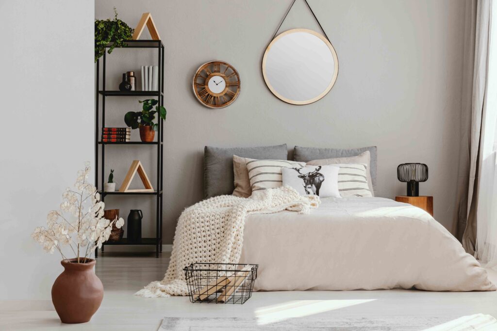 Picture of a bedroom with hygge interior design, including a black bookshelf, a round mirror and a basket of books by the bed